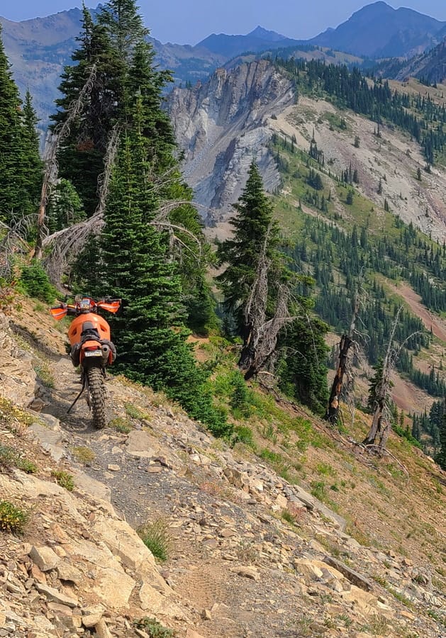 motorcycle parked on a narrow trail on the side of a mountain
