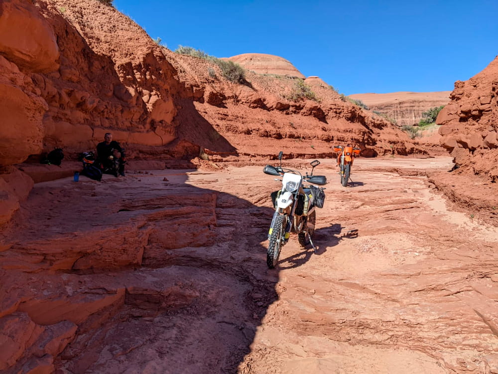 two motorcycles parked in a canyon and a rider sittin in shade