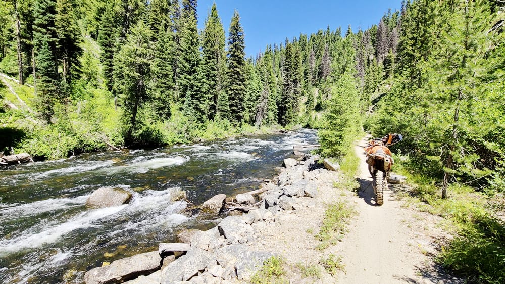 motorcycle paked on a trail next to a gushing river