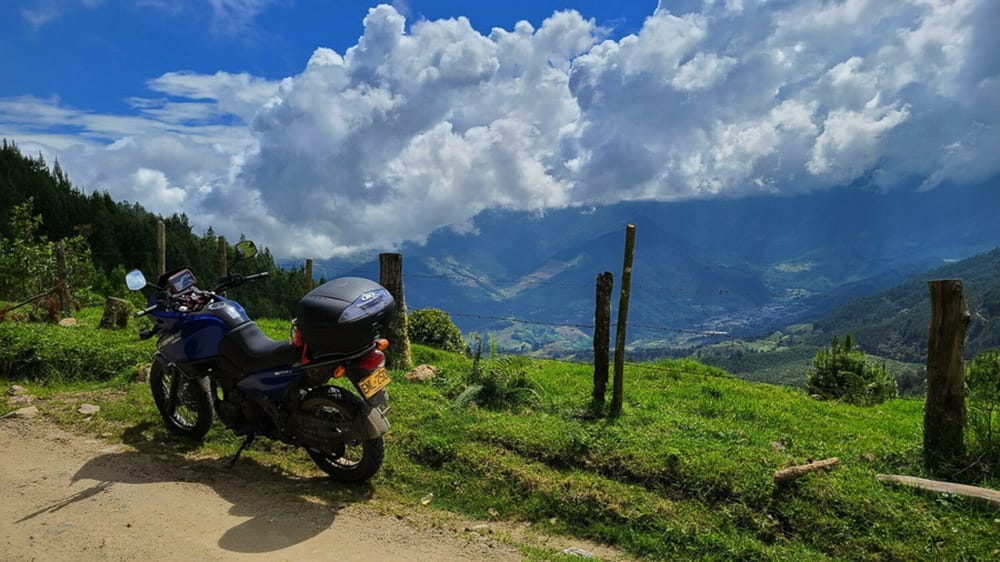 motorcycle parked with a deep valley and fluffy clouds behind  