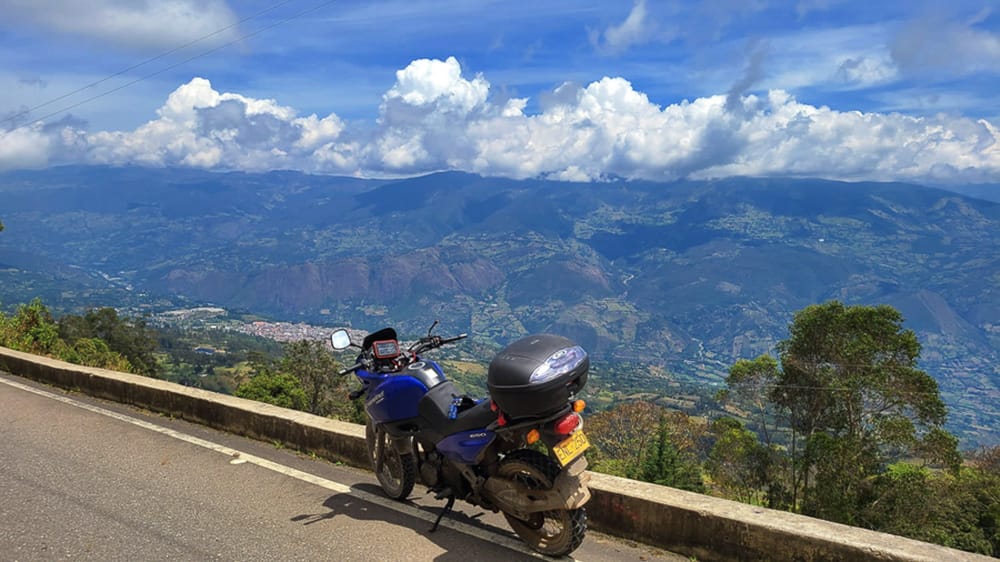 motorcycle parked on a road high up in mountains and a town below