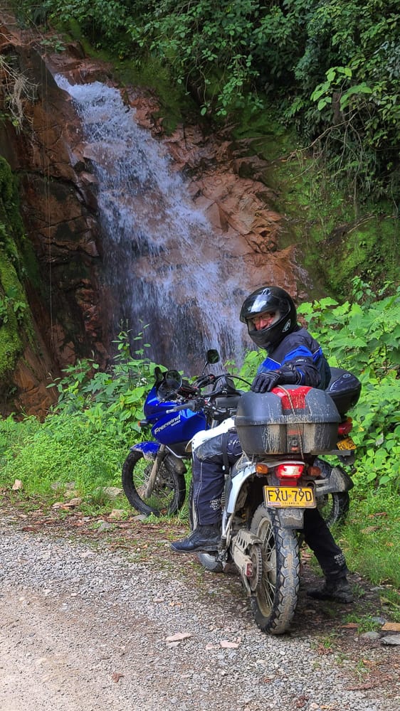  rider and two motorcycles in front of a waterfall