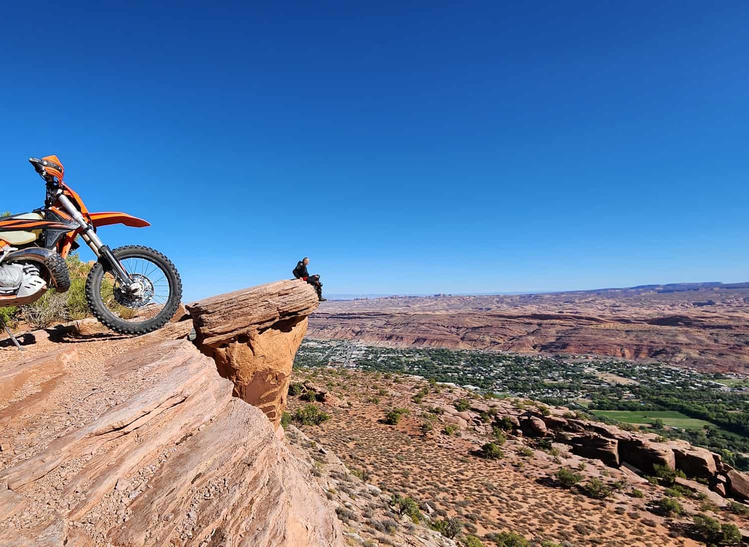 rider sitting at the edge of a cliff, high above a green valley
