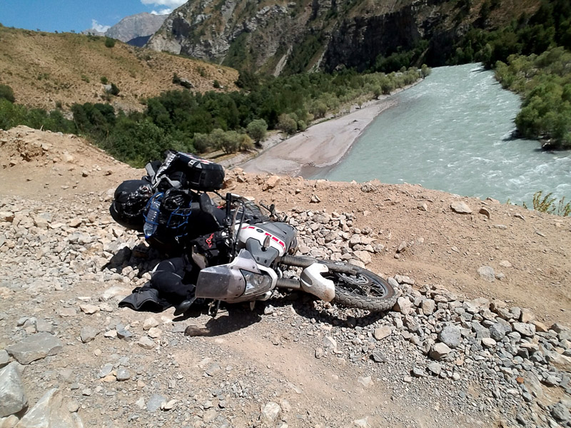 fallen motorcycle on a dirt road and raging river below