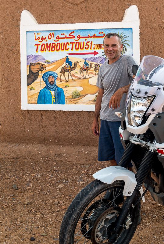 posing next to a wall sign to Tombouctou