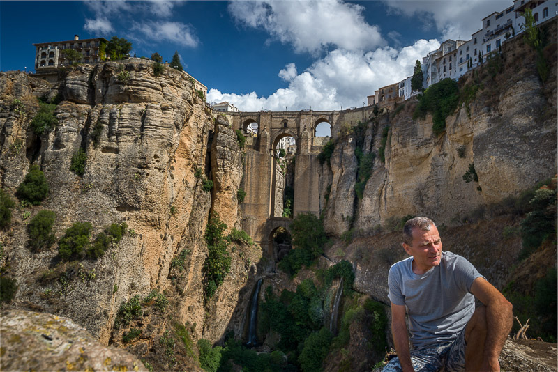 sitting in a canyon with a high stone bridge behind