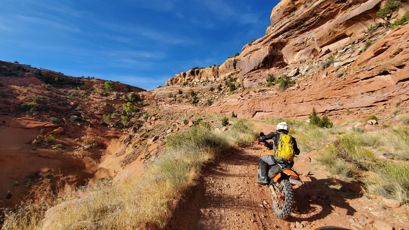 rider going up a narrow dirt road next to cliffs