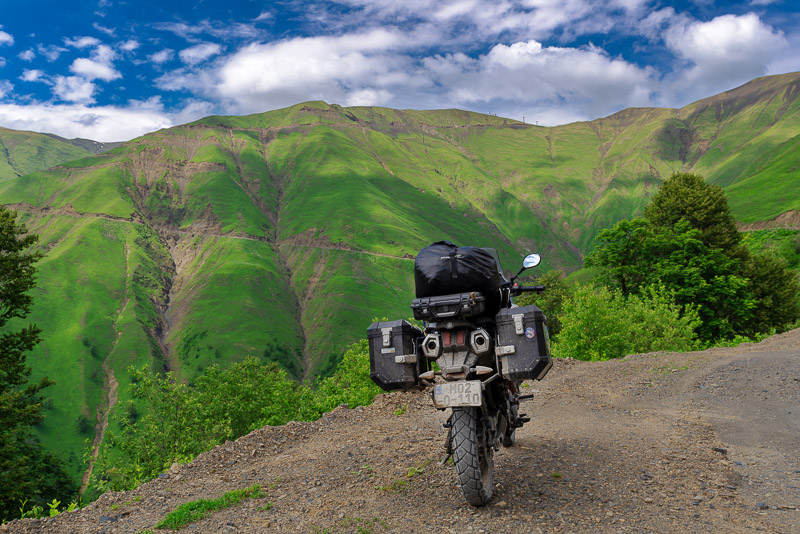 motorcycle parked on a dirt road going up a high mountain behind