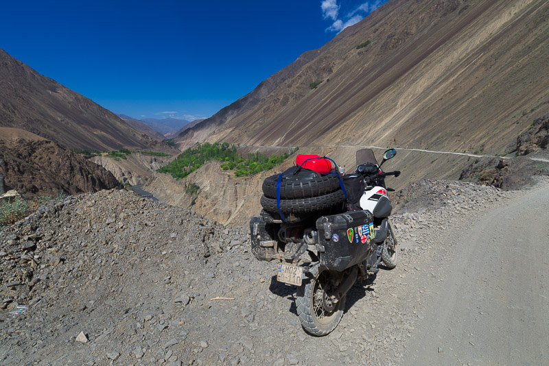 loaded motorcycle parked on a dirt road going through a valley