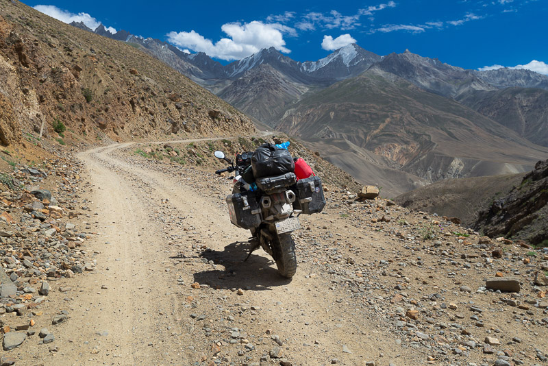 motorcycle parked on a dirt road snaking up a steep mountain side with deep canyon on one side