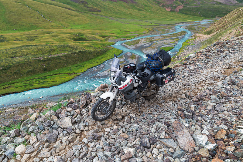 motorcycle parked on a narror rocky road with creek far below