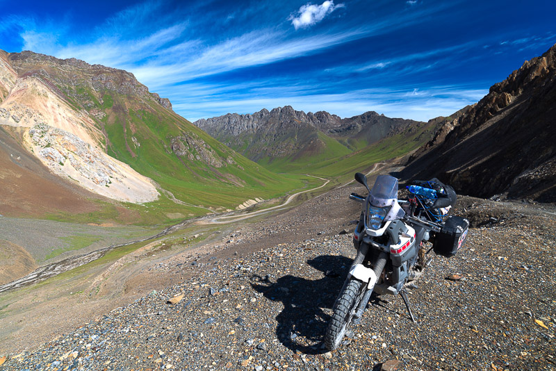 motorcycle parked on a dirt road with green valley below