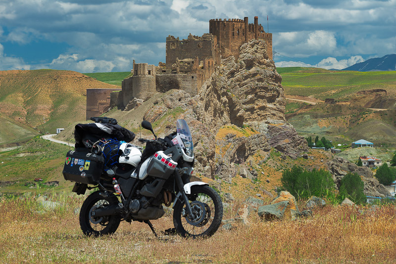 motorcycle parked on a grassy hill with a fortress behind