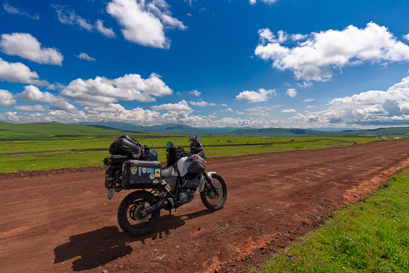motorcycle parked on a dirt road with fluffy clouds above
