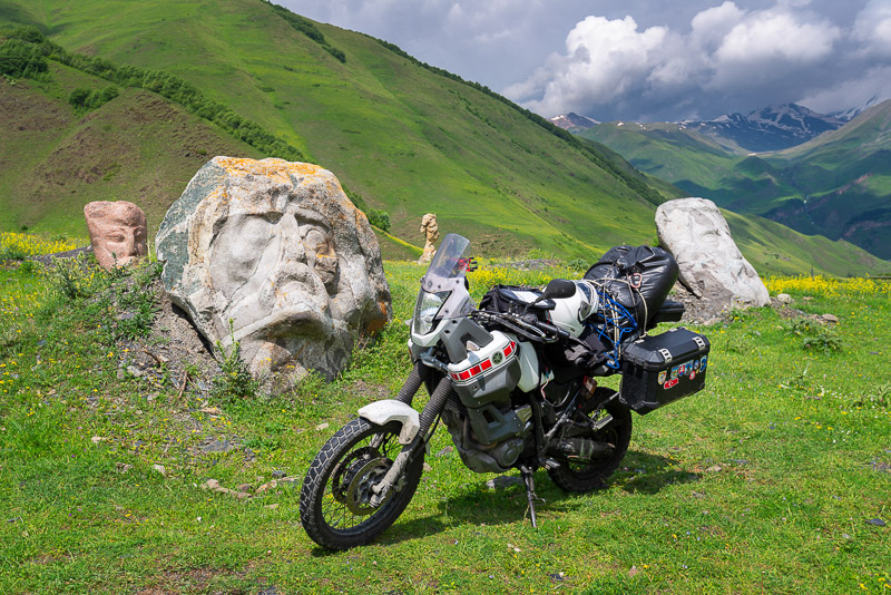 motorcycle parked next to big rocks with faces carved on them