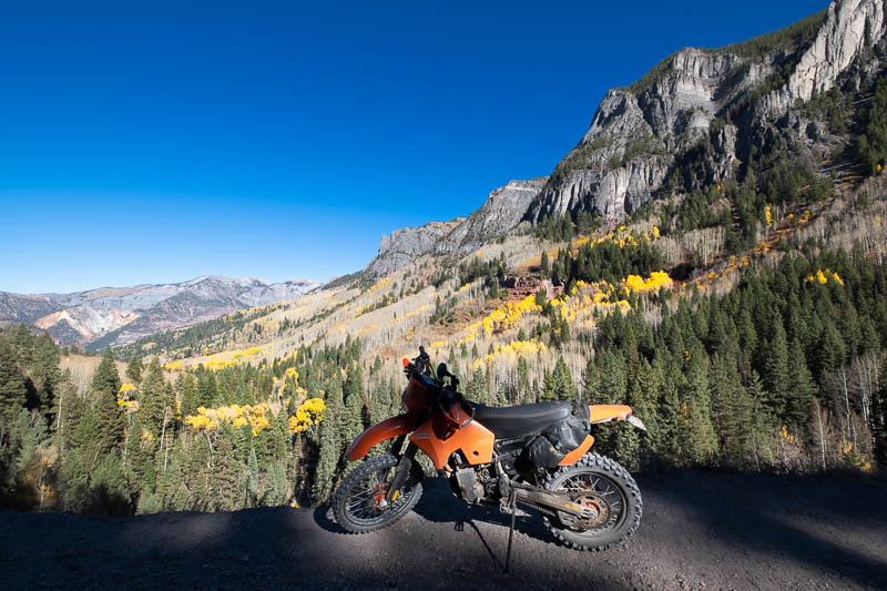 motorcycle parked in a canyon with pine trees and yellow aspens behind