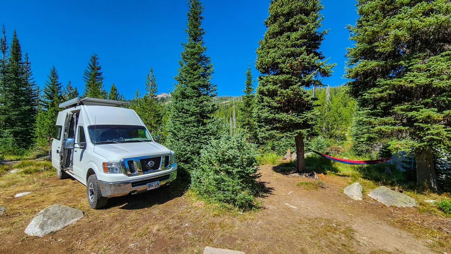 camp with van and hammoc among pine trees