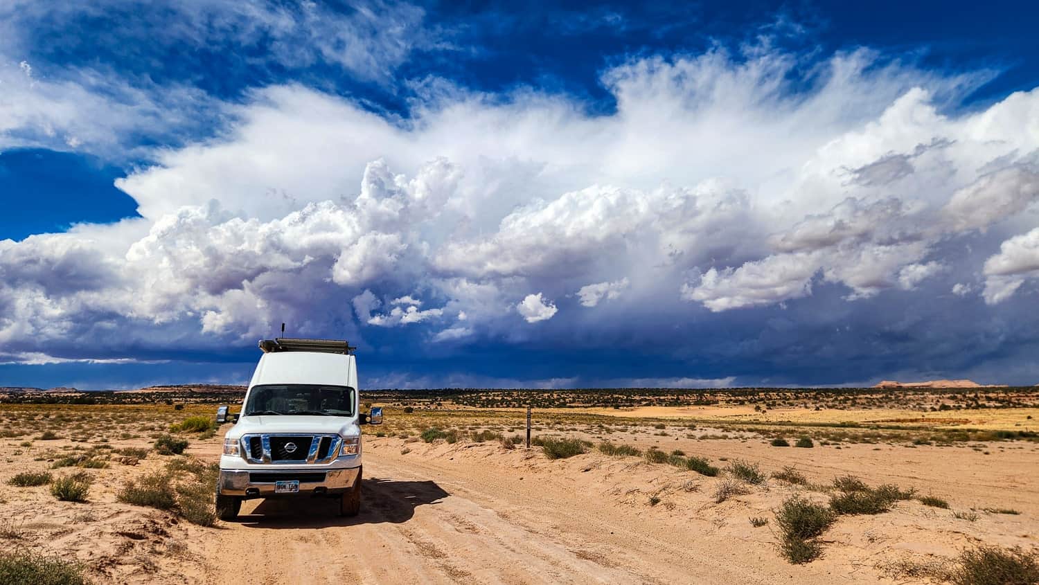 van parked on a desert road with stormy clouds behind